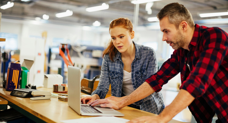 Young man and young woman using a laptop while working in a printing press office