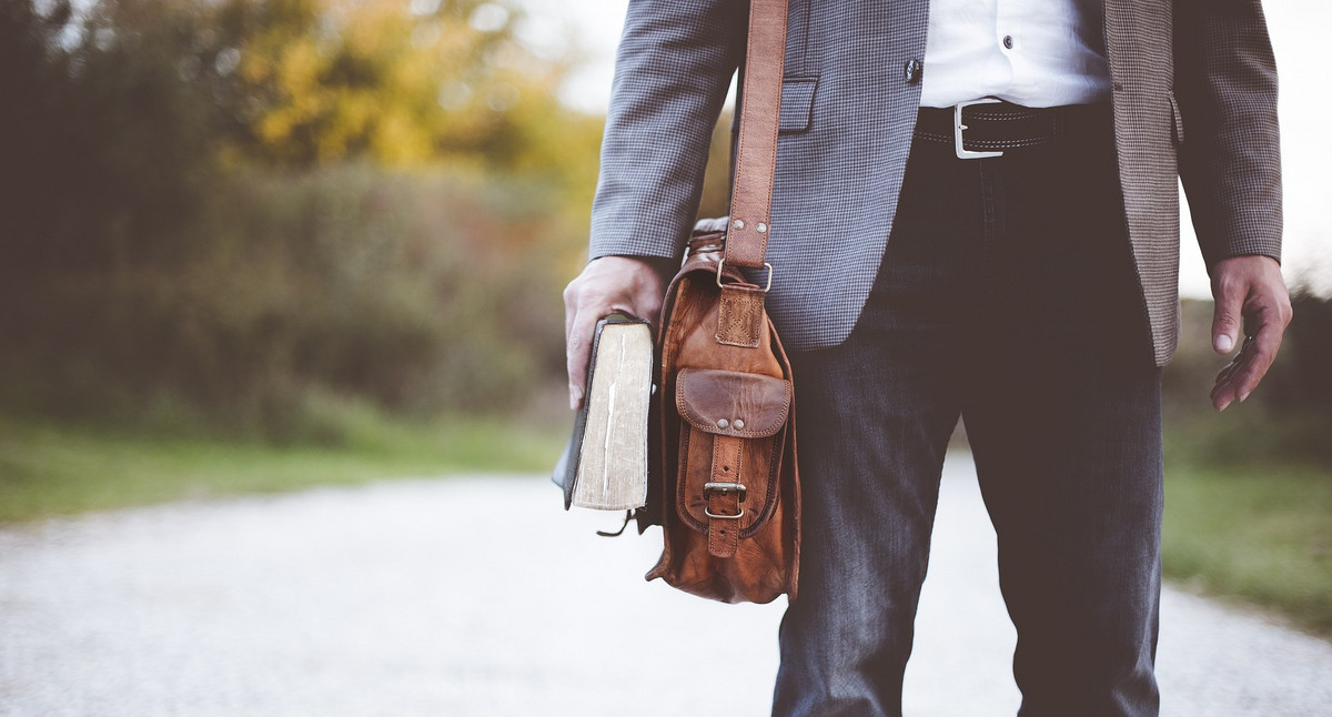 Symboldbild: Eine Person mit einer Aktentasche und einem Buch in der Hand