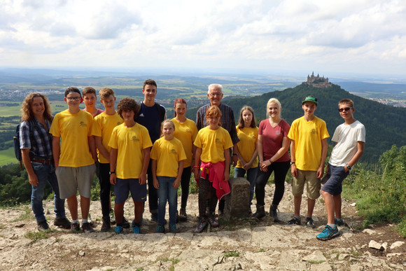 Sommertour Kretschmann wandert mit Bürgerinnen und Bürgern Gruppenbild mit Ministerpräsident Winfried Kretschmann (M.) und der Schwäbischen Albvereinsjugend auf dem Zeller Horn, im Hintergrund die Burg Hohenzollern