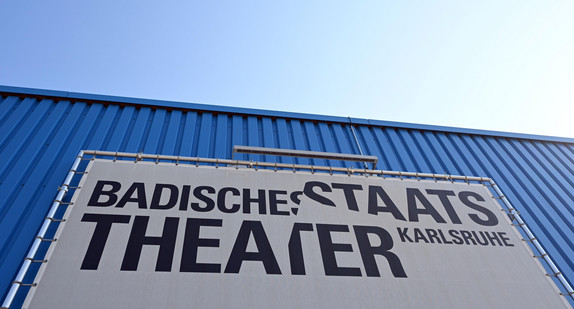 Vor dem Badischen Staatstheater hängt ein Plakat mit dem Schriftzug "Badisches Staatstheater Karlsruhe".