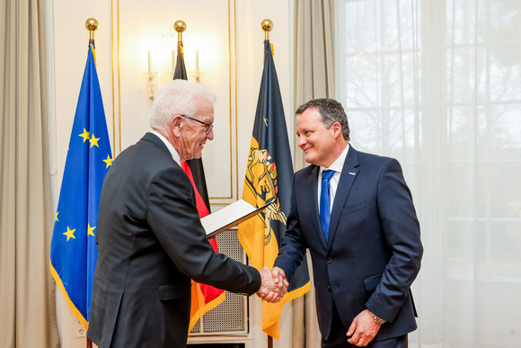 Auszeichnung Staufermedaille in Gold für Thomas Speidel Ministerpräsident Winfried Kretschmann (links) überreicht Thomas Speidel (rechts) die Staufermedaille in Gold. Im Hintergrund stehen Fahnen.