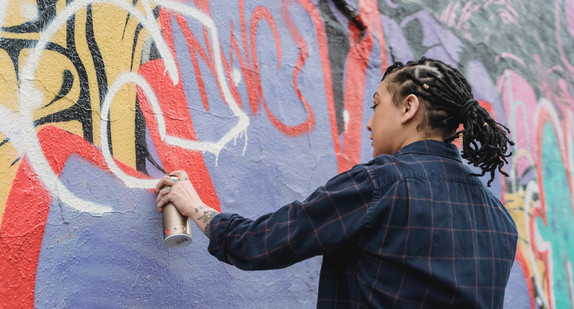 Symbolbild, eine Frau sprüht Graffiti an eine Hauswand