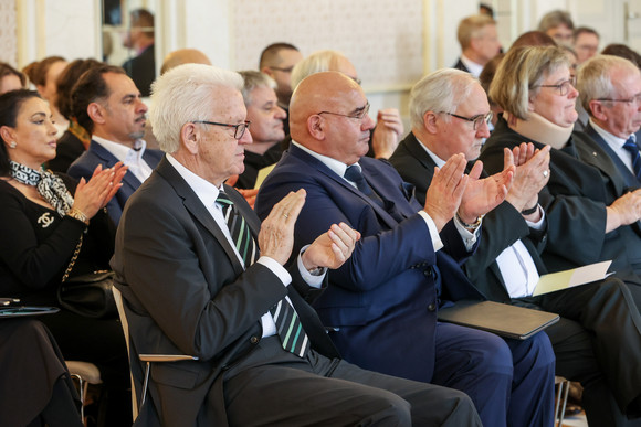 Gedenkveranstaltung 80. Jahrestag der Deportation von Sinti und Roma Ministerpräsident Winfried Kretschmann (vorne links) und Daniel Strauß (vorne, zweiter von links), Landesvorsitzender des Verbands Deutscher Sinti und Roma, sitzen im Publikum und applaudieren.
