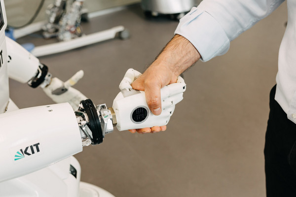 Auf dem Foto sind ein Roboter und ein Mensch zu sehen, die sich die Hände schütteln