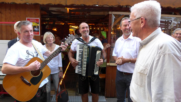 Sommertour Kretschmann wandert mit Bürgerinnen und Bürgern Kirchheimer Weindorf: Ministerpräsident Winfried Kretschmann (r.) mit Musikanten und Gästen