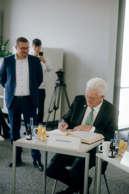 Schulbesuch Austausch zu Reformen für weiterführende Schulen Pfullingens Bürgermeister Stefan Wörner (links, stehend) und Ministerpräsident Winfried Kretschmann (rechts, sitzend) beim Eintrag in das Gästebuch