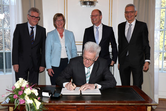 Besoldung Mehr Geld für Beamte Ministerpräsident Winfried Kretschmann (sitzend) unterzeichnet die Vereinbarung; stehend v.l.n.r.: Volker Stich, Vorsitzender des Beamtenbundes Baden-Württemberg, Finanzministerin Edith Sitzmann, Matthias Grewe, Vorsitzender des Vereins der Richter und Staatsanwälte Baden-Württemberg e.V., und Staatssekretär Martin Jäger