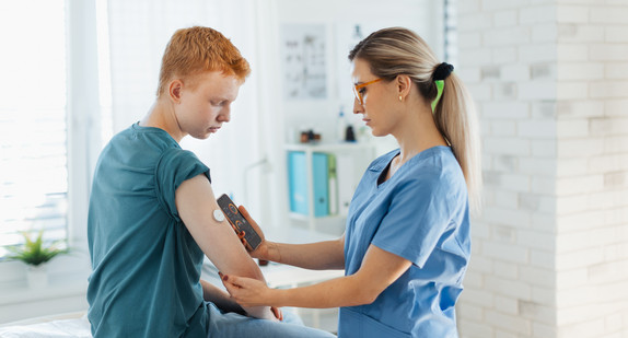 Diabetologist doctor connecting continuous glucose monitor sensor to smartphone, checking teenage boy's glucose data in real time. Endocrinologist taking care of teenage diabetic patient.
