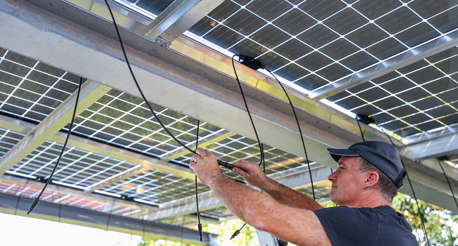Ein Mann installiert Solarzellen auf dem Dach eines Carports.']